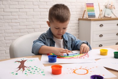 Photo of Little boy painting with finger at wooden table in room