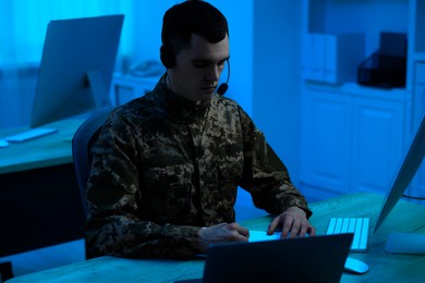 Military service. Soldier in headphones working at wooden table in office at night