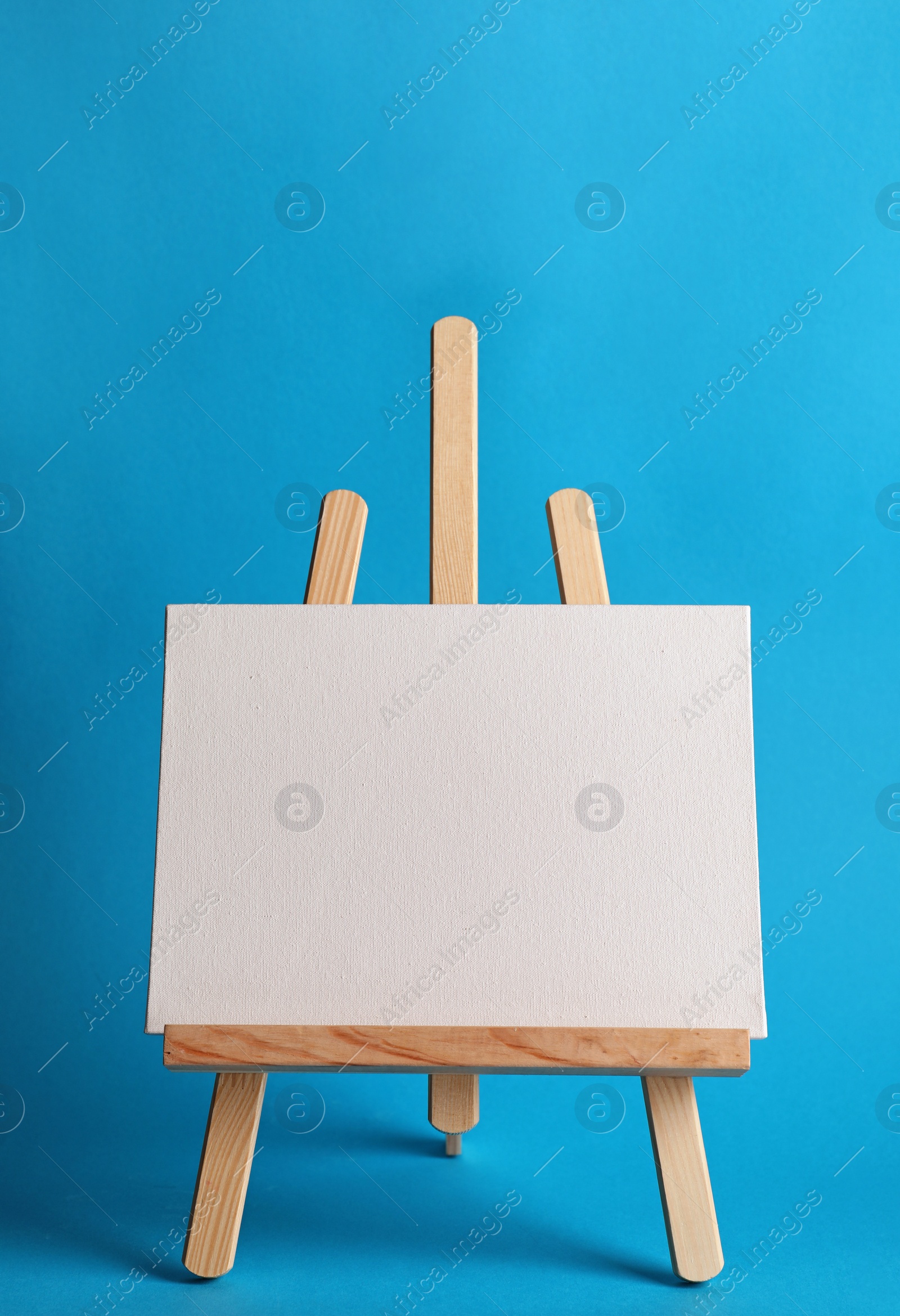 Photo of Wooden easel with blank canvas board on color background. Children's painting