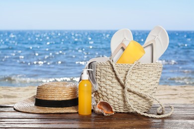 Image of Stylish bag and other beach accessories on wooden table near sea