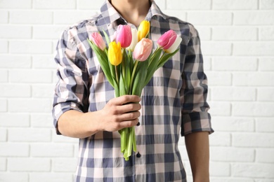 Photo of Man holding bouquet of beautiful spring tulips near brick wall, closeup. International Women's Day