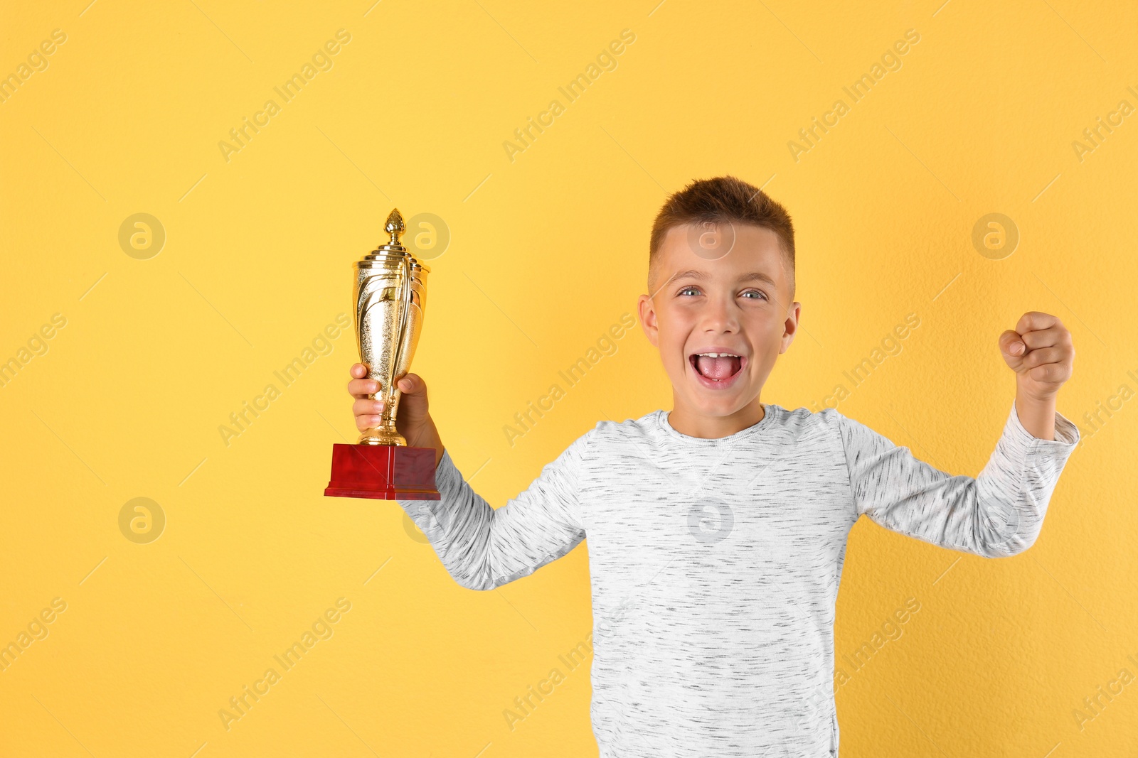 Photo of Happy boy with golden winning cup on yellow background