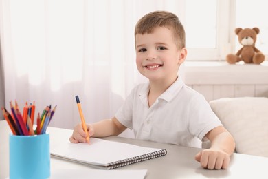 Photo of Cute little boy drawing with pencil at grey table in room. Child` art