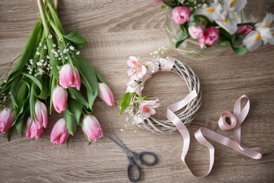 Decorator's workplace with unfinished wreath and beautiful flowers, top view