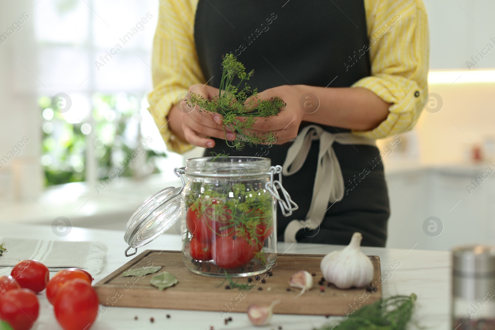 Photo of Woman putting dill into pickling jar at table in kitchen, closeup