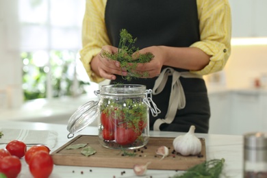 Woman putting dill into pickling jar at table in kitchen, closeup