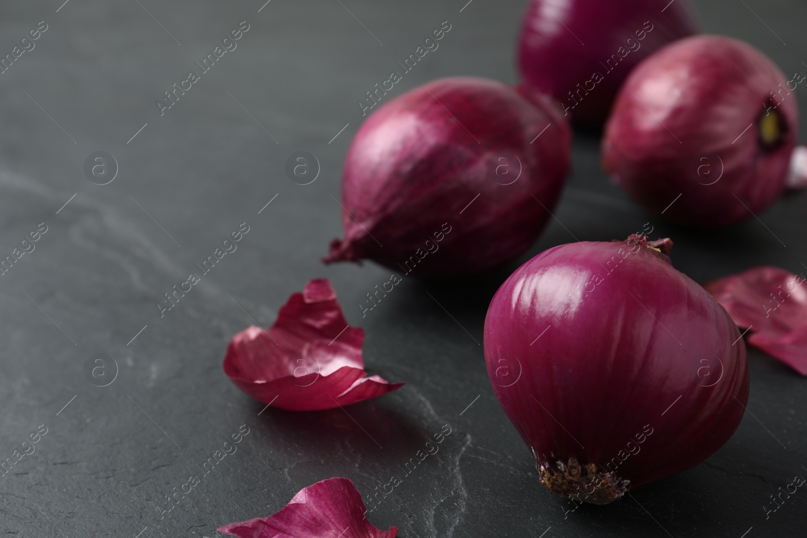 Photo of Ripe red onion bulbs on black slate table, closeup