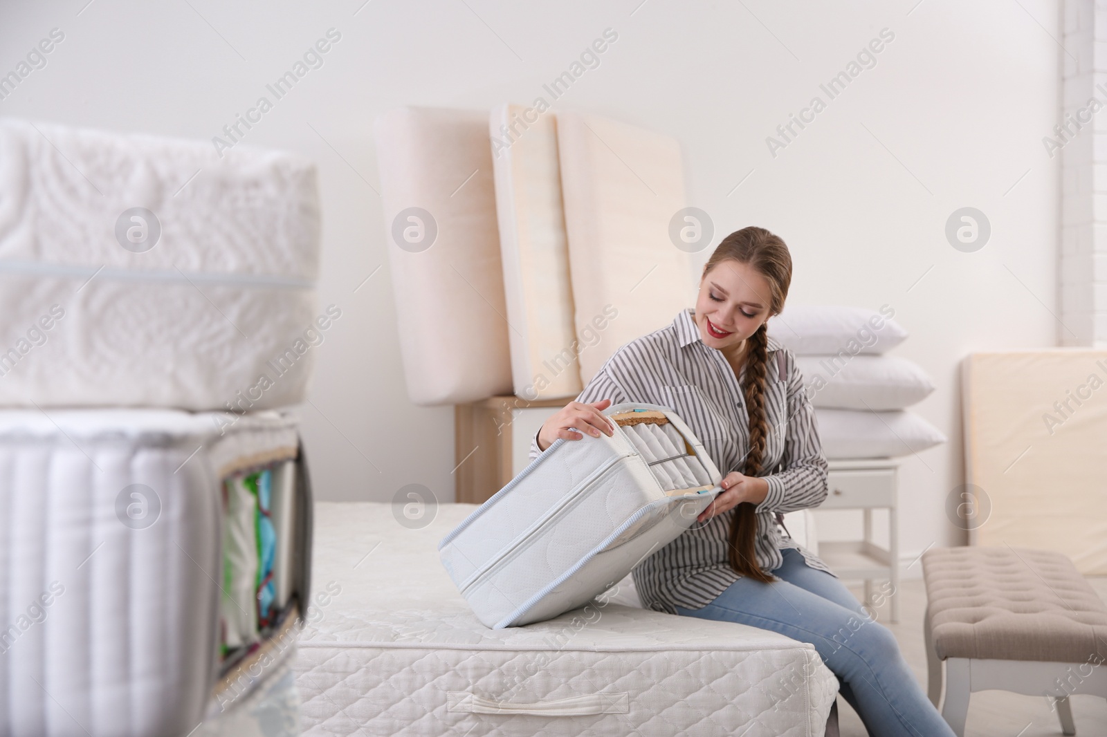 Photo of Young woman choosing mattress in furniture store