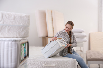 Photo of Young woman choosing mattress in furniture store