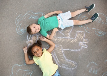 Photo of Little children lying near chalk drawing of airplane on asphalt, top view
