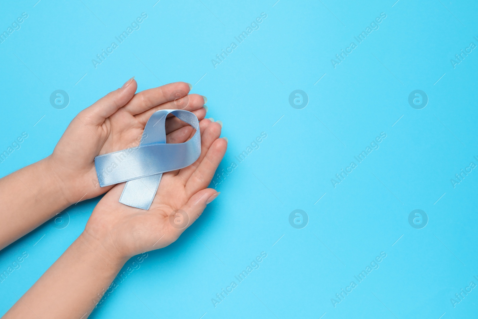 Photo of Woman holding light blue awareness ribbon on color background, top view. Space for text