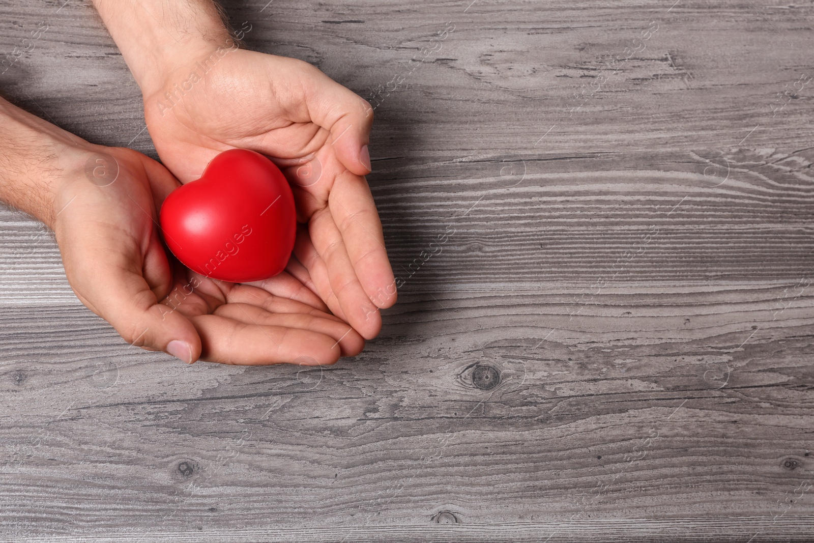 Photo of Young man holding red heart on grey wooden background, top view with space for text. Donation concept