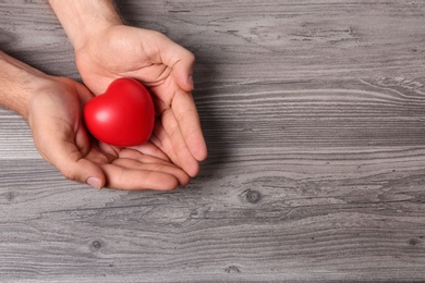 Photo of Young man holding red heart on grey wooden background, top view with space for text. Donation concept