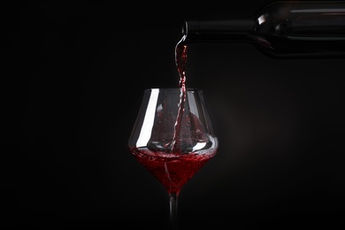 Photo of Pouring wine from bottle into glass on black background