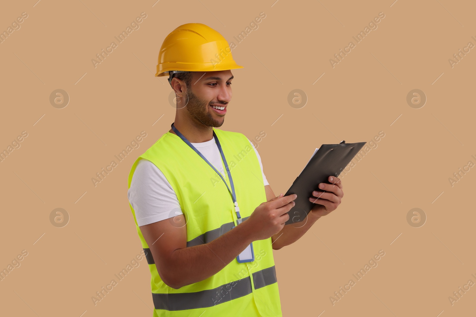 Photo of Engineer in hard hat holding clipboard on beige background