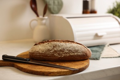 Wooden bread basket and freshly baked loaf on white marble table in kitchen