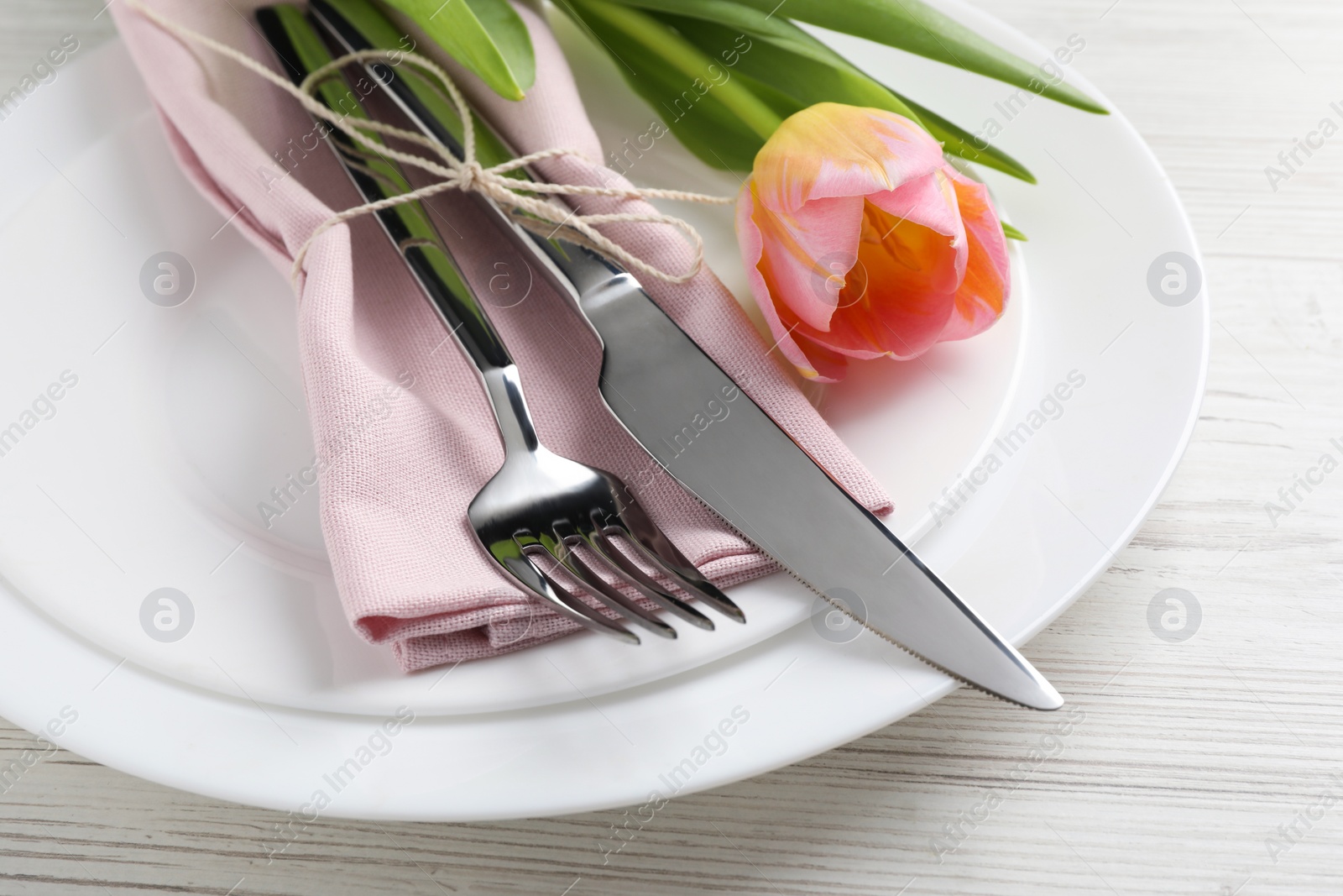 Photo of Stylish table setting with cutlery and tulip on white wooden background, closeup