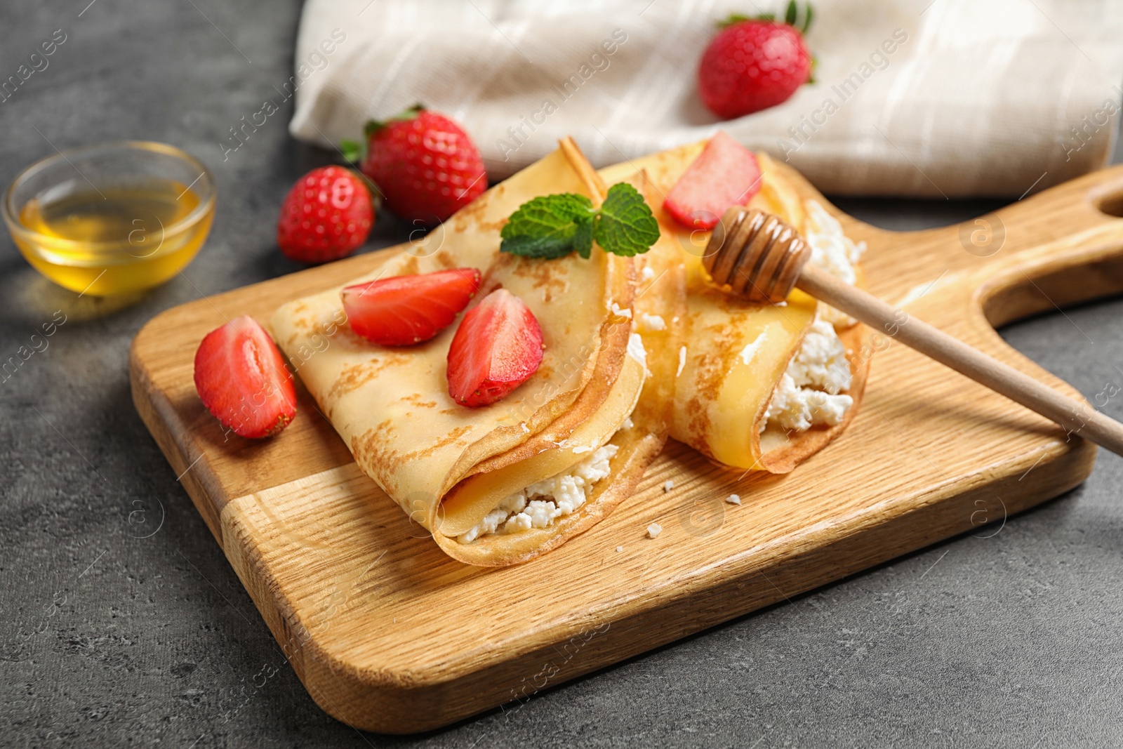 Photo of Delicious thin pancakes with strawberries, cottage cheese and honey on grey table