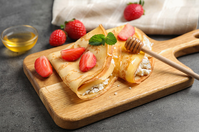 Delicious thin pancakes with strawberries, cottage cheese and honey on grey table