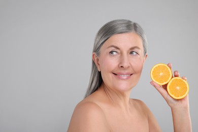 Photo of Beautiful woman with halves of orange rich in vitamin C on grey background, space for text