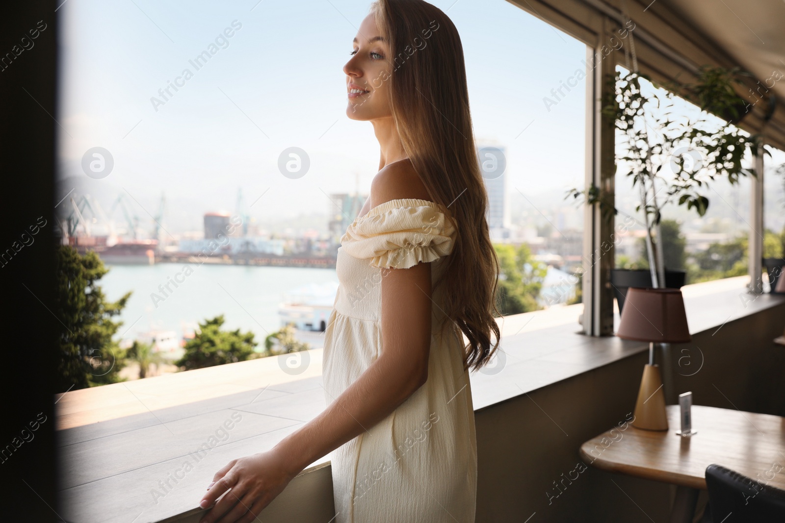 Photo of Beautiful young woman standing on balcony, space for text