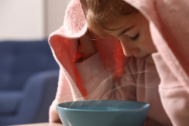 Photo of Little girl covering head with towel and inhaling steam indoors, closeup