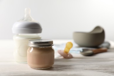 Photo of Jar with healthy baby food and bottle of milk on white wooden table. Space for text