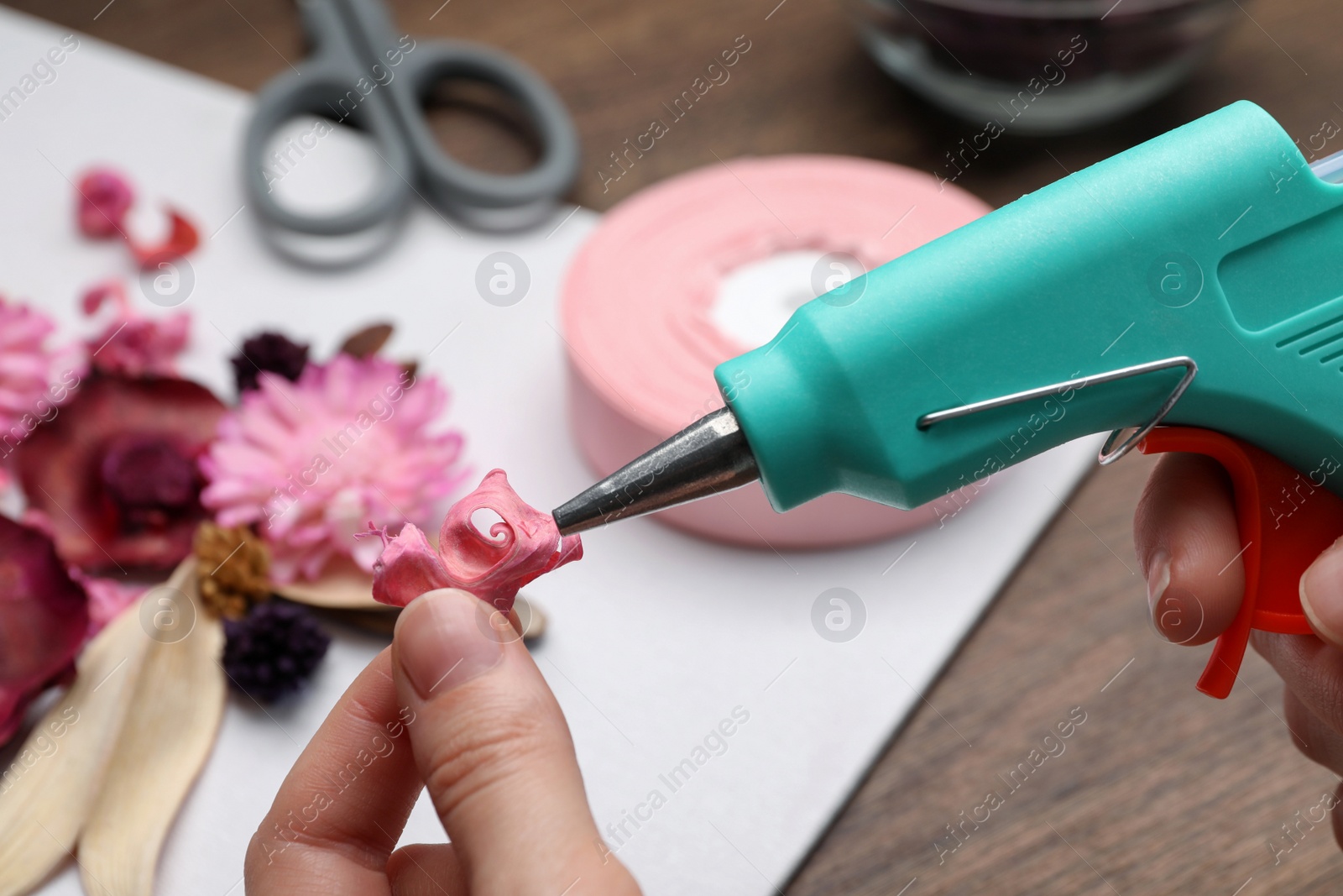 Photo of Woman using hot glue gun to make craft at wooden table, closeup