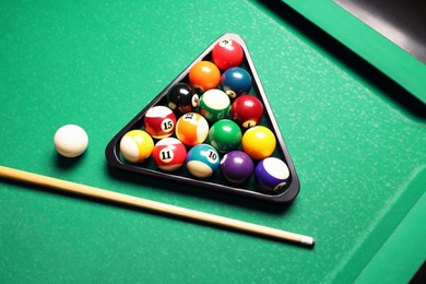 Plastic triangle rack with billiard balls and cue on green table