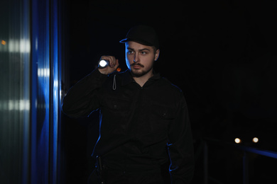 Male security guard with flashlight in dark corridor