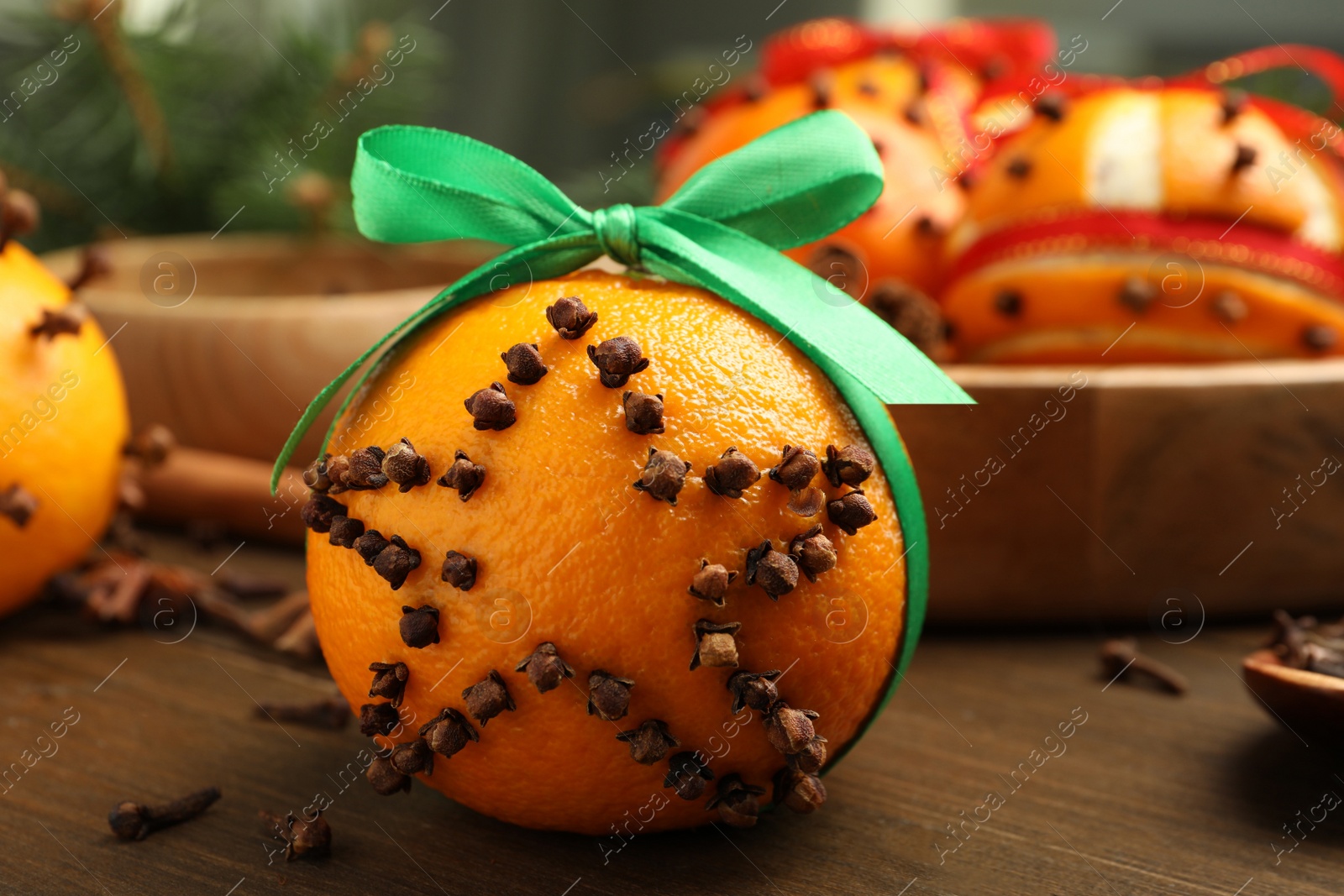 Photo of Pomander ball with green ribbon made of fresh tangerine and cloves on wooden table