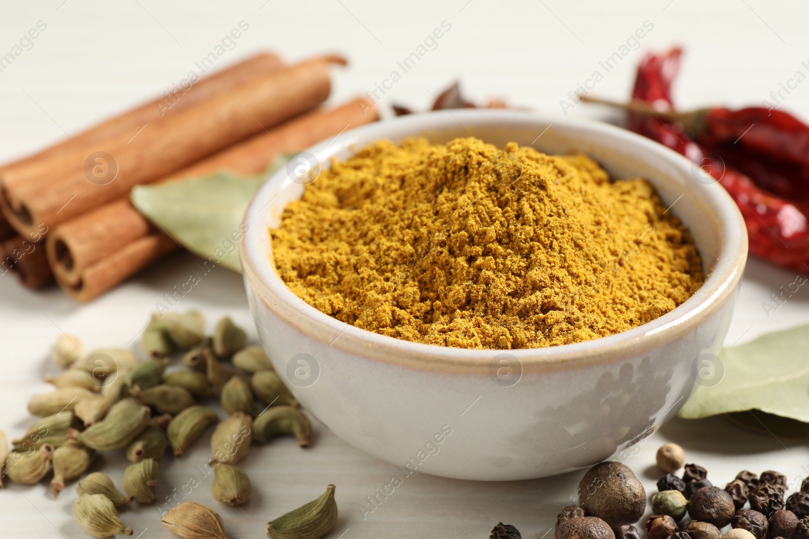 Photo of Curry powder in bowl and other spices on white wooden table, closeup