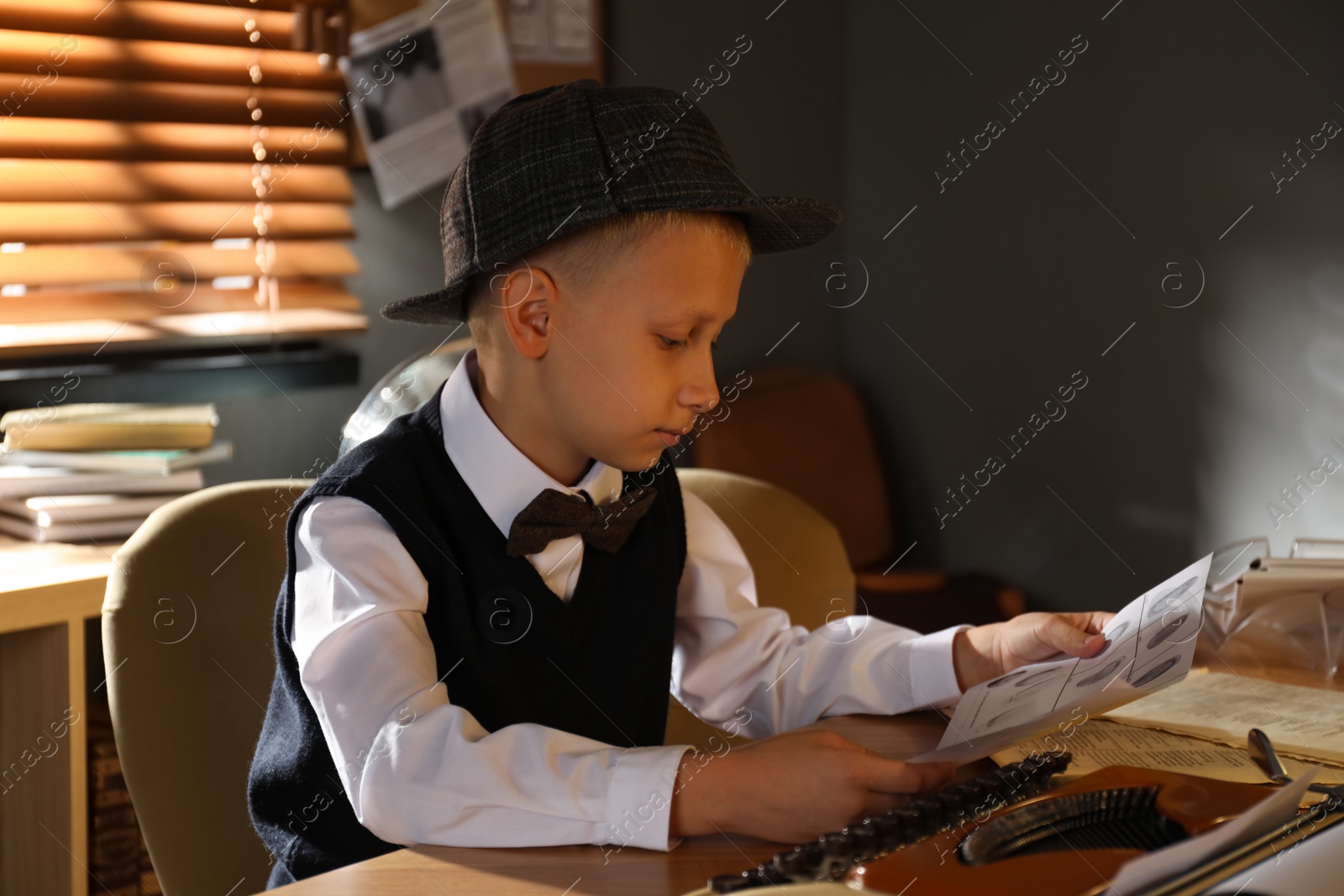 Photo of Cute little detective with fingerprints card at table in office