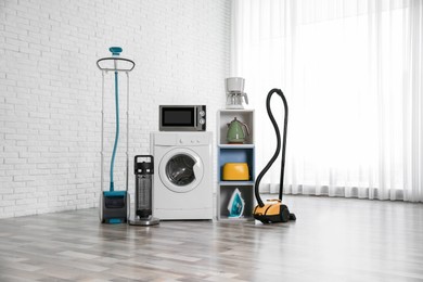Photo of Modern vacuum cleaner and different household appliances near window indoors