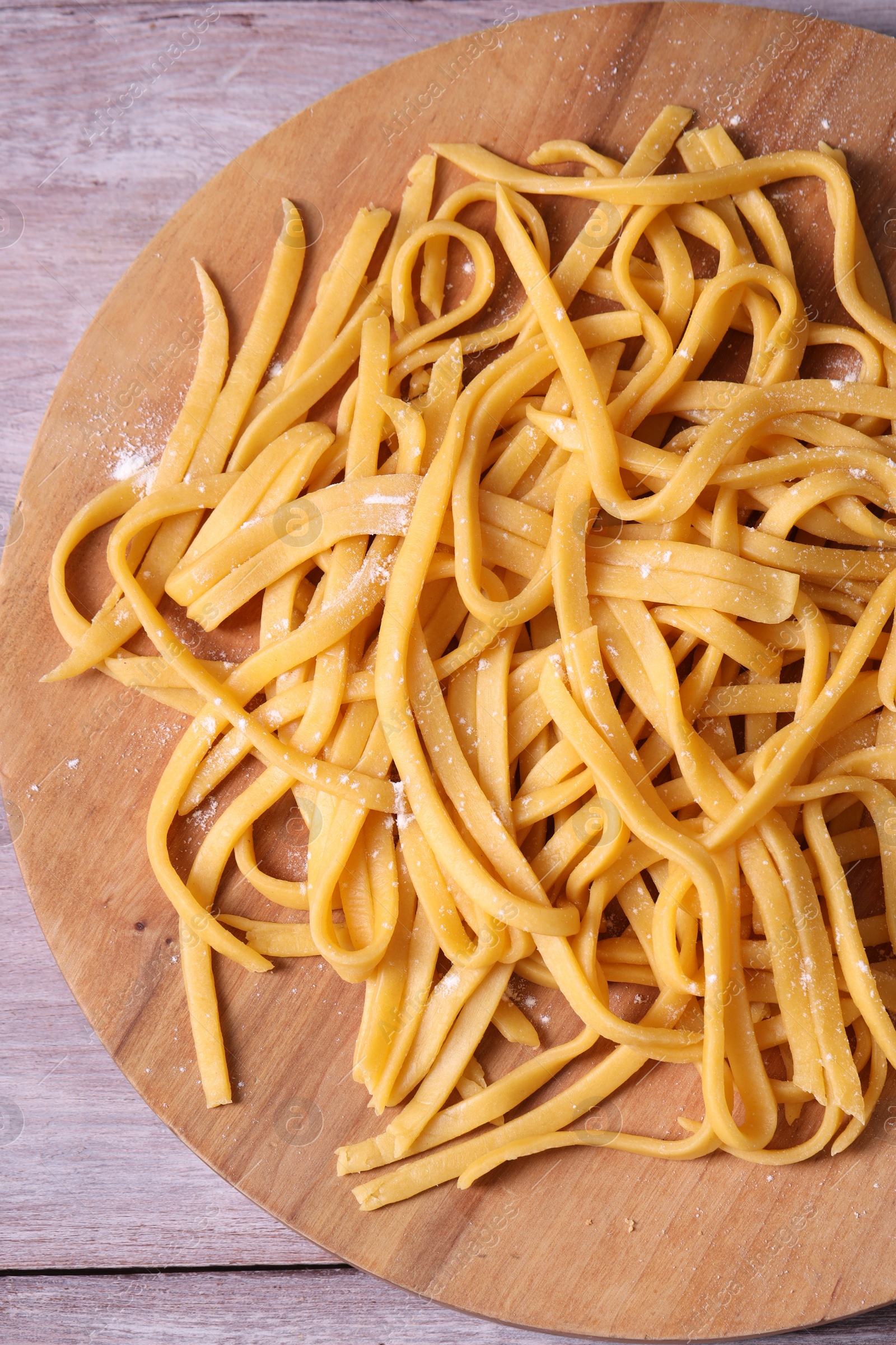 Photo of Board with homemade pasta on wooden table, top view