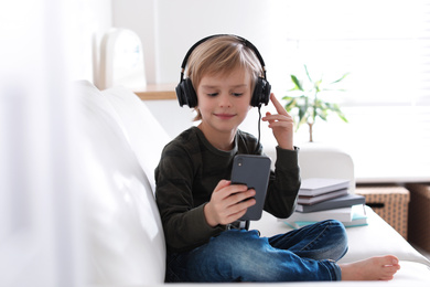 Cute little boy with headphones and smartphone listening to audiobook at home