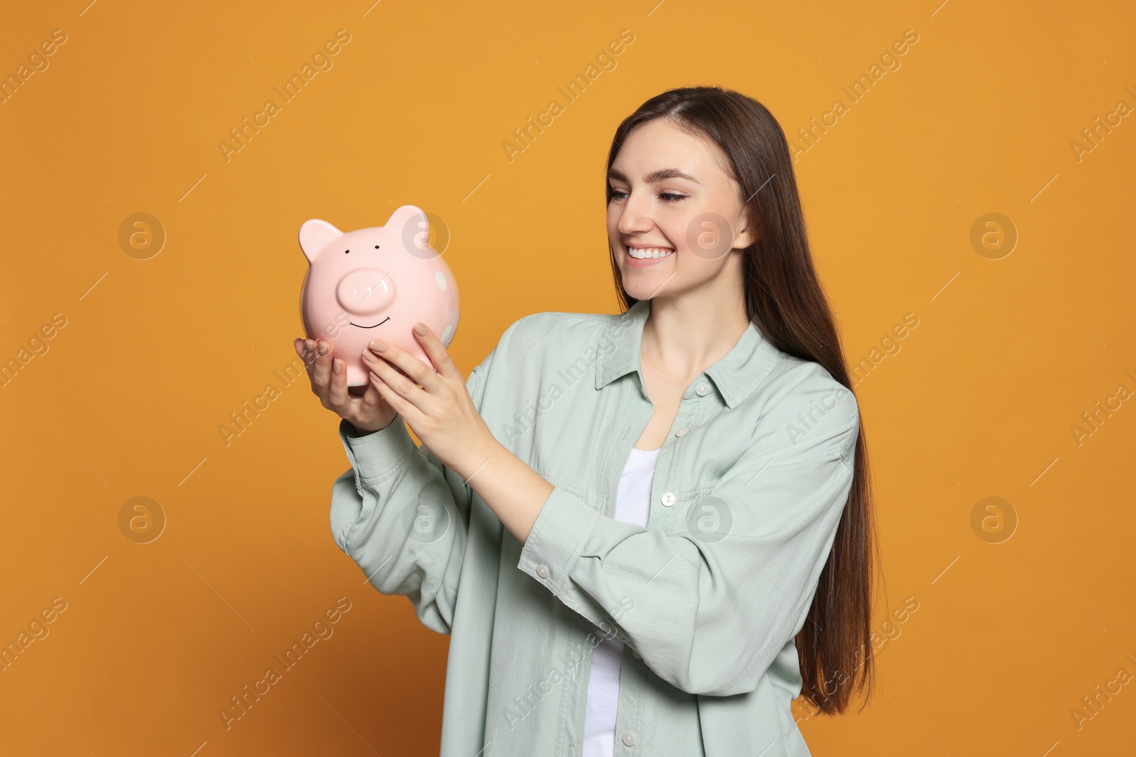 Photo of Happy young woman with piggy bank on orange background