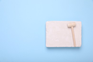 Photo of Educational toy for motor skills development. Excavation kit (plaster and wooden mallet) on light blue background, top view with space for text