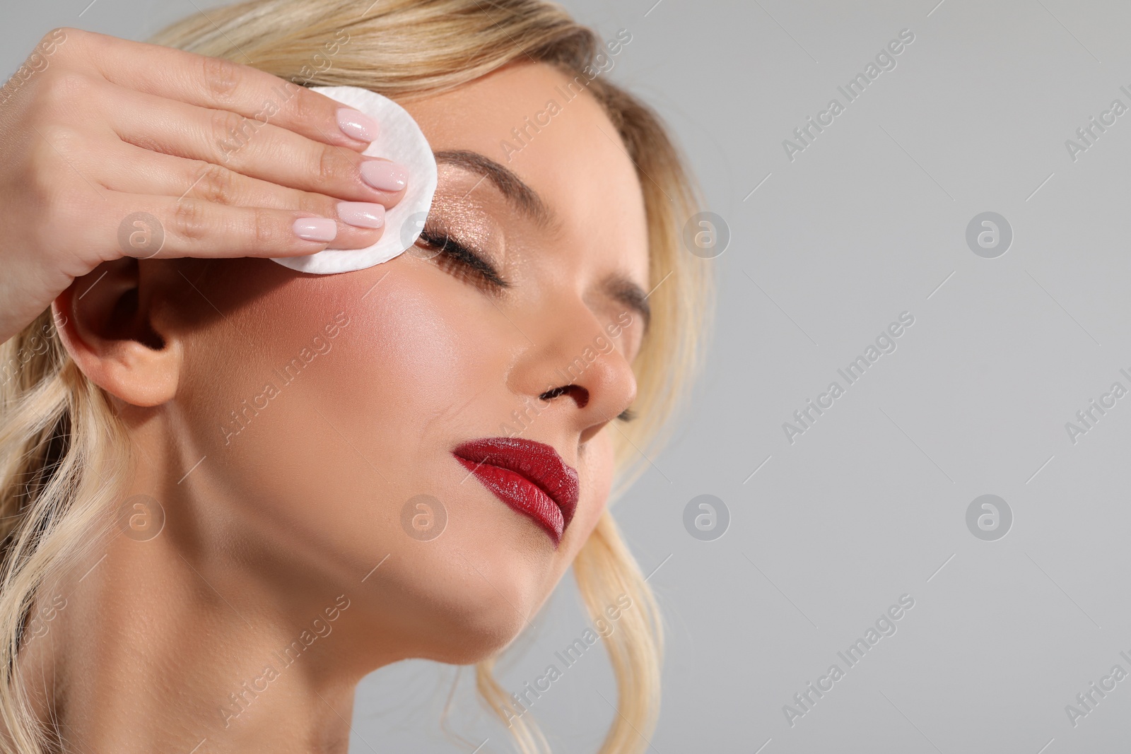 Photo of Beautiful woman removing makeup with cotton pad on light grey background, closeup. Space for text