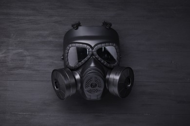 Photo of One gas mask on black wooden background, top view