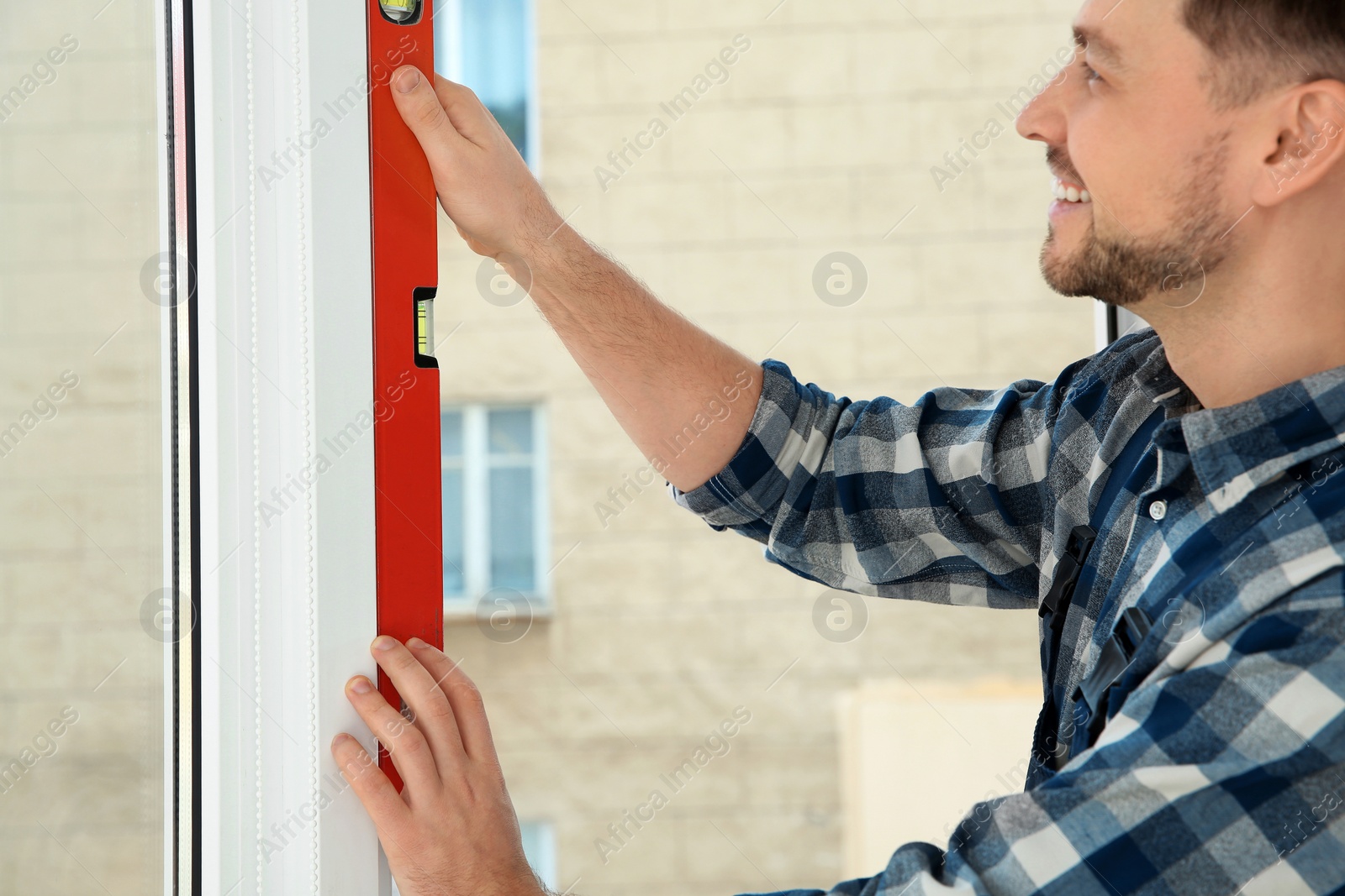 Photo of Construction worker using bubble level while installing window indoors, closeup