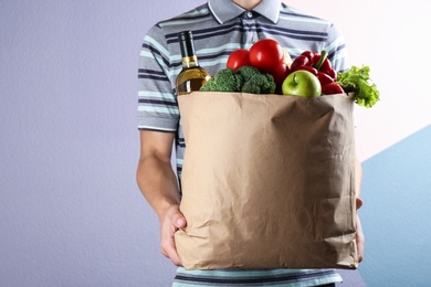 Man holding paper bag with different groceries near color wall, closeup view. Space for text