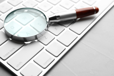 Photo of Magnifier glass and keyboard on light grey stone background, closeup. Find keywords concept