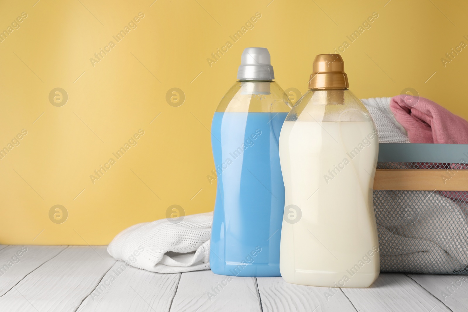 Photo of Bottles of fabric softener and clothes in basket on white wooden table, space for text