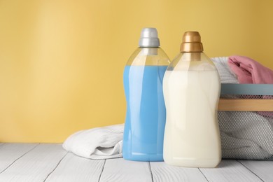 Photo of Bottles of fabric softener and clothes in basket on white wooden table, space for text