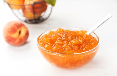 Bowl with peach jam and spoon on table