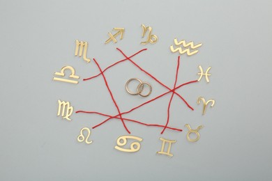 Photo of Zodiac compatibility. Signs, red threads and wedding rings on grey background, flat lay