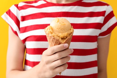 Woman holding tasty ice cream in wafer cone on yellow background, closeup