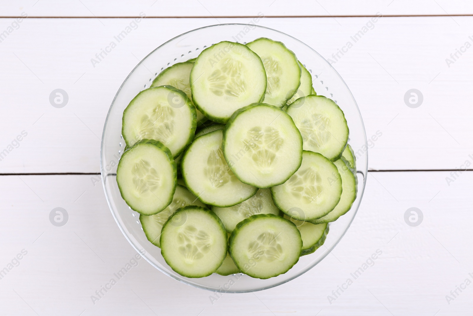 Photo of Cut cucumber in bowl on white wooden table, top view