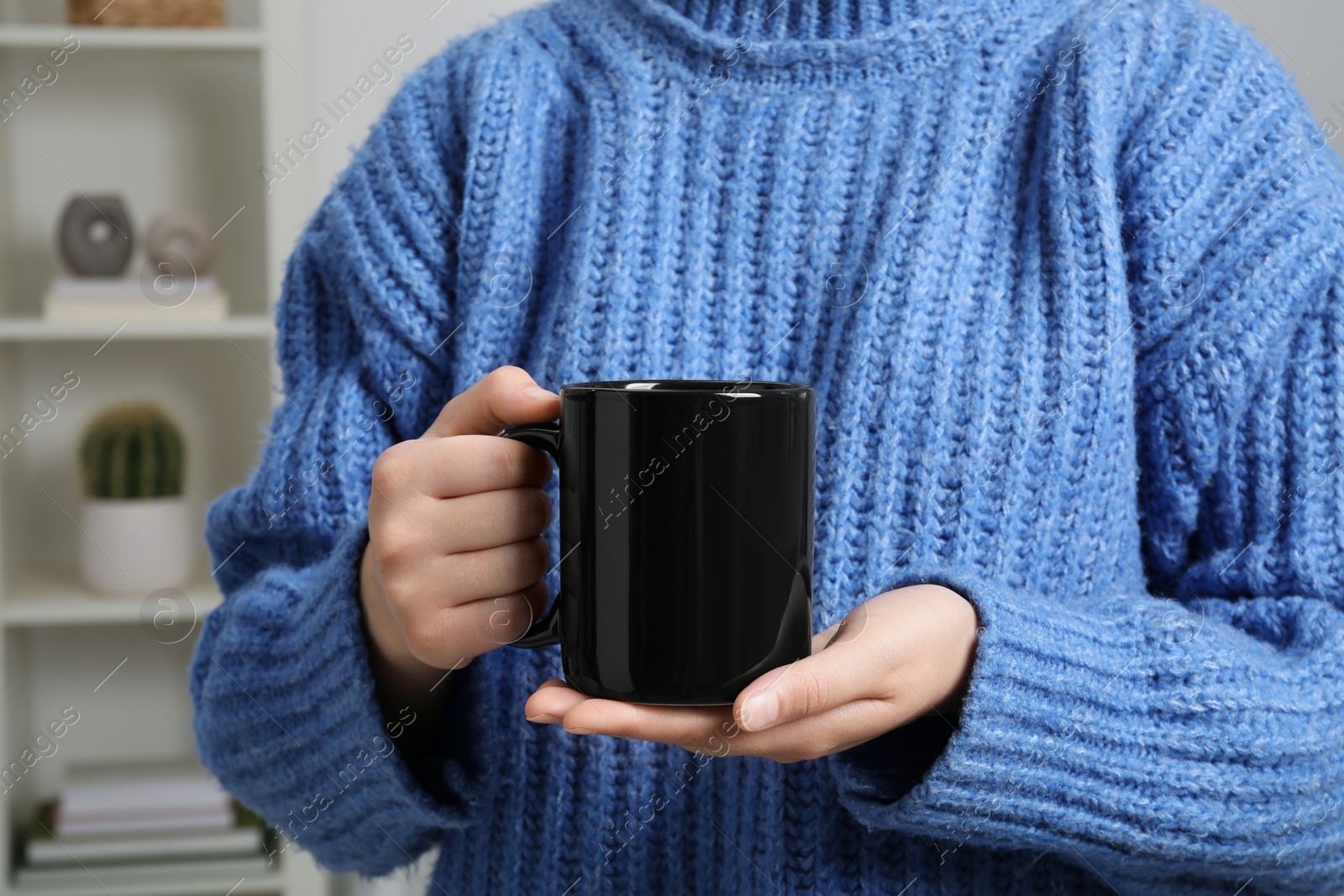 Photo of Woman holding black mug at home, closeup. Mockup for design